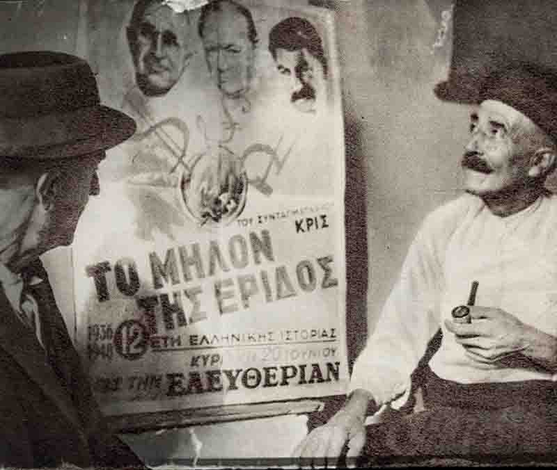 Two men seated in front of a political poster, engaged in conversation, with a focus on the poster's message.