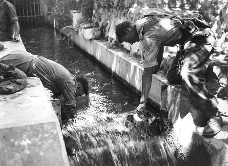 Vintage print of two British soldiers actively catching water from a stream, visualizing a realistic approach to obtaining drinking water.