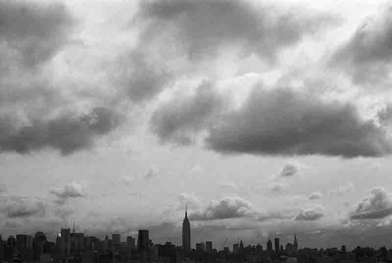 A black and white fine art photograph showcasing the Manhattan skyline, featuring distinct building outlines and a dramatic contrast between light and shadow.