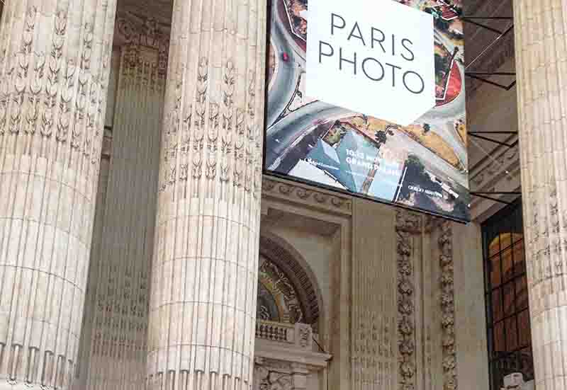 Large Paris Photo exhibition banner hanging between the ornate stone columns at the entrance of the Grand Palais in Paris.