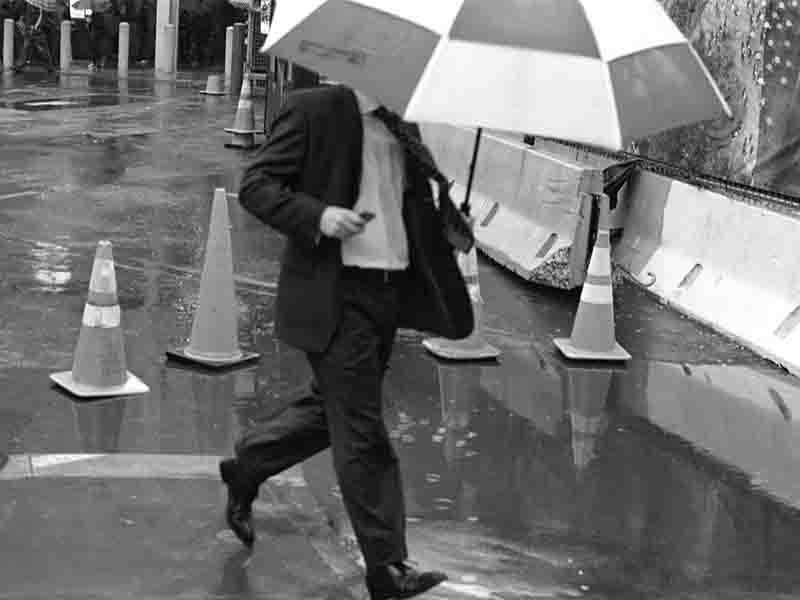 A well-dressed man in a suit and tie strides through the rain, holding an umbrella to shield himself from the downpour.